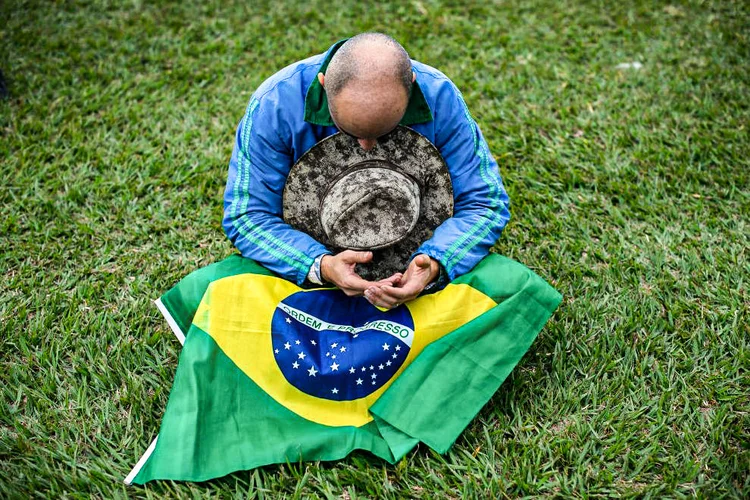 Economia brasileira: homem sentado na grama com bandeira do Brasil no colo (Andressa Anholete/Getty Images)