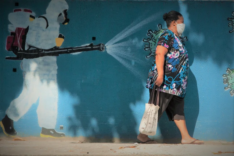 A woman wearing a protective mask is seen walking in front of graffiti by collectives of artists Nogenta and contraconsiencia, in the neighborhood of Estácio in central Rio de Janeiro,  on June 12, 2020.  The graffiti depict a man performing a disinfection and the face of President Jair Bolsonaro represented by a virus. (Photo by Allan Carvalho/NurPhoto via Getty Images) (Allan Carvalho/NurPhoto/Getty Images)