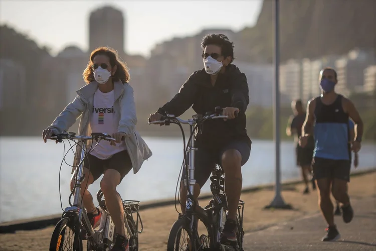 RIO DE JANEIRO, BRAZIL - JUNE 17: Cyclists wearing face masks ride by the Rodrigo de Freitas Lagoon amidst the coronavirus (COVID-19) pandemic on June 17, 2020 in Rio de Janeiro, Brazil. The city of Rio de Janeiro started today the second phase of the quarantine flexibilization. The decree determines the return of 100% of the bus fleet and some commercial establishments following distance rules such as reduced opening hours, restricting the flow of people and maintaining hygiene standards. (Photo by Andre Coelho/Getty Images) (Andre Coelho/Getty Images)