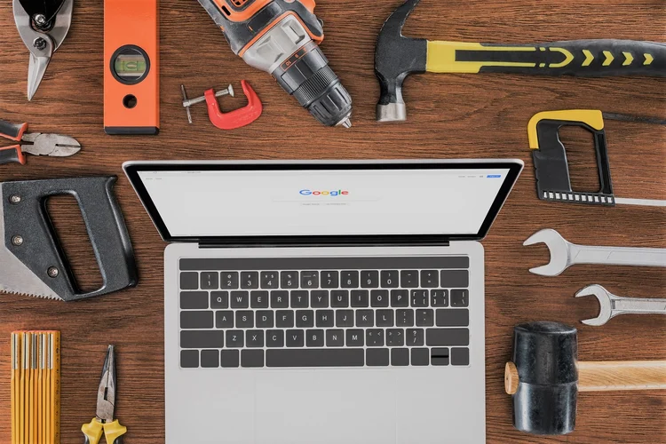 top view of workplace with laptop with google on screen surrounded by various tools on wooden table (LightFieldStudios/Getty Images)