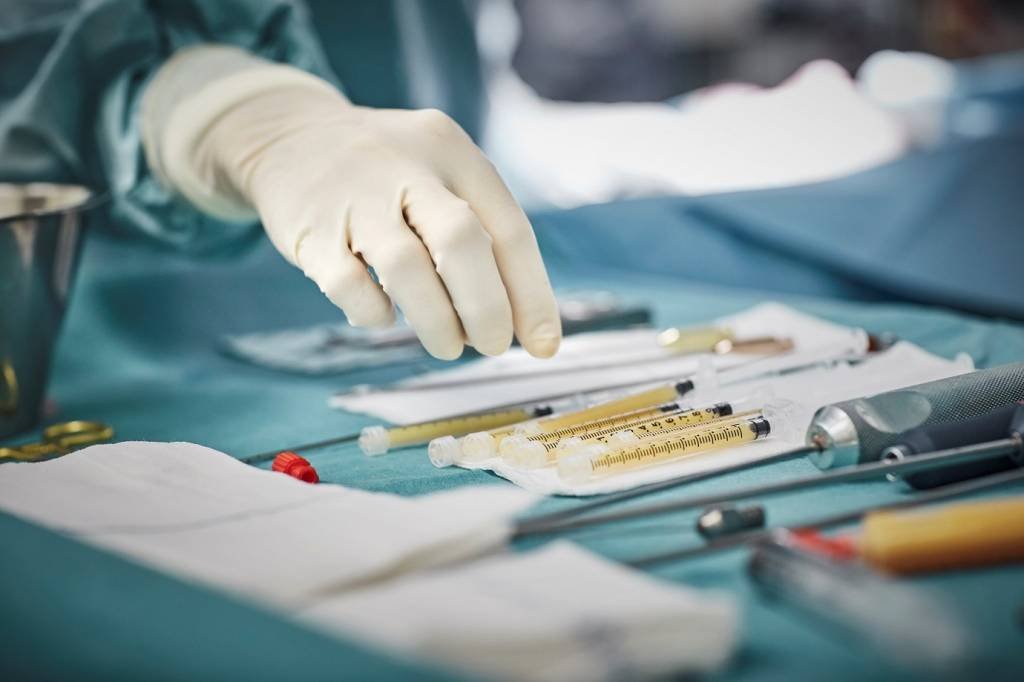 Cropped image of female surgeon reaching for syringes on table. Close-up of healthcare worker's hand wearing surgical glove. She is in emergency room. (Morsa Images/Getty Images)