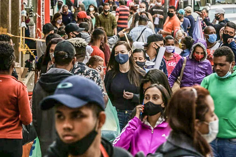 Pessoas de máscaras andam em uma rua movimentada no centro da cidade de SP (Alexandre Schneider/Getty Images)