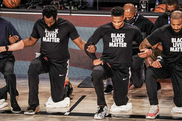 Jogadores do Houston Rockets e do Dallas Mavericks se ajoelham de braços dados durante execução do hino nacional, em partida pela NBA em 31/7/2020: NBA difere de NHL e NFL (Mike Ehrmann/Getty Images)