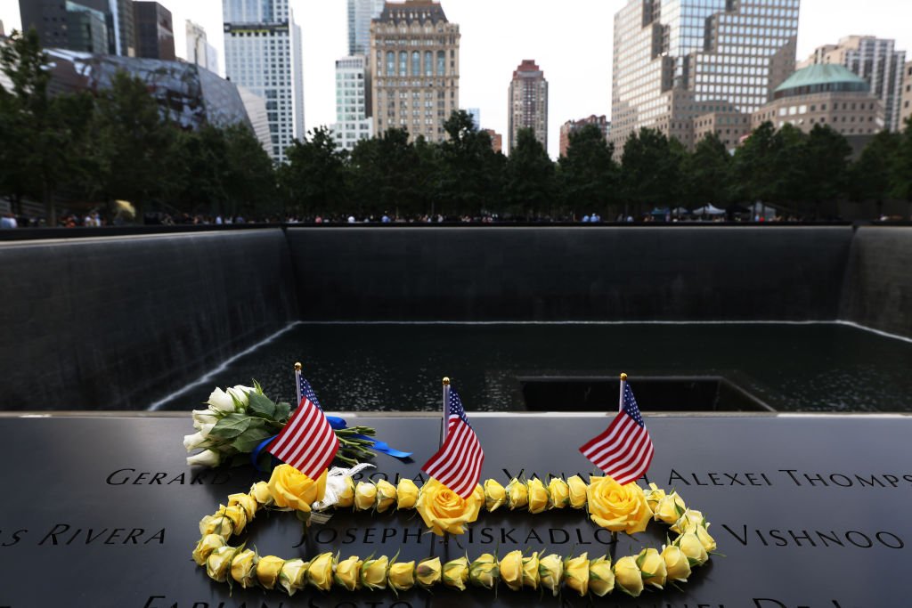 NEW YORK, NEW YORK - SEPTEMBER 11: Flowers and American flags surround are placed around a name during a 9/11 memorial service at the National September 11 Memorial and Museum on September 11, 2020 in New York City. The ceremony to remember those who were killed in the terror attacks 19 years ago will be altered this year in order to adhere to safety precautions around COVID-19 transmission. (Photo by Michael M. Santiago/Getty Images)