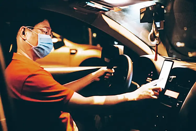 Image of Asian male E-hailing driver with face mask using smartphone to received order. (simon2579/Getty Images)