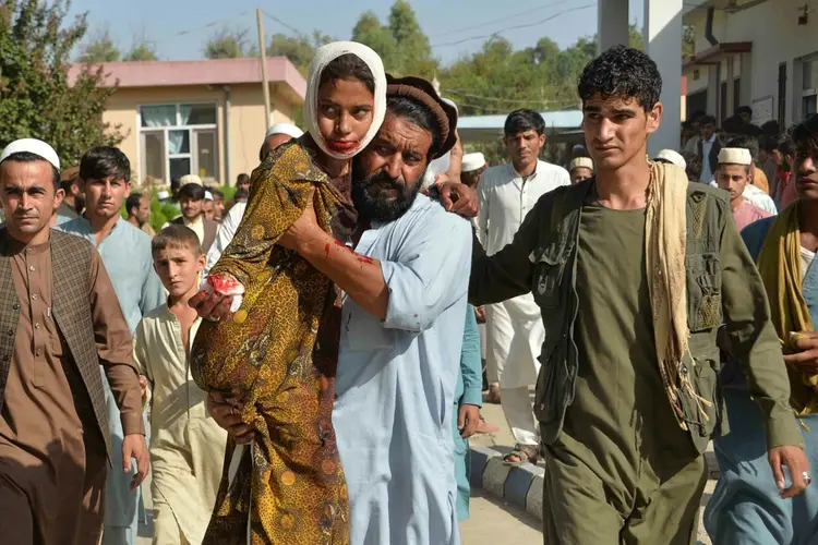 Homem carrega menina ferida em ataque com carro-bomba no distrito de Ghani Khel, na província afegã de Nangarhar (Divulgação/AFP)