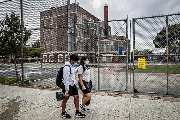 Pessoas caminham com máscaras faciais em frente à Public School, fechada no bairro Queens de Nova York, EUA (Shannon Stapleton/Reuters)