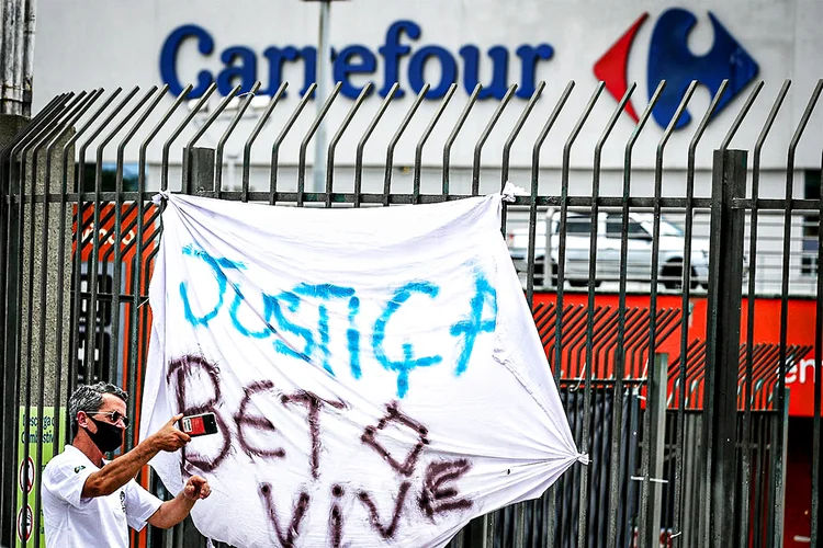 Homem tira foto em frente a faixa de protesto contra a morte de João Alberto Silveira Freitas, morto por espancamento por seguranças em loja do Carrefour em Porto Alegre (Diego Vara/Reuters)