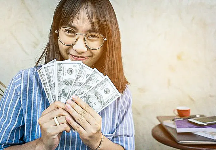 Jovem sorrindo e segurando dinheiro
 (Jidpipat Taewiriyakun / EyeEm/Getty Images)