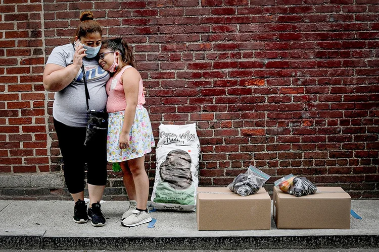 Cidadã norte-americana desempregada e sua filha aguardam carona após receberem alimentos gratuitos de instituição em Massachusetts, nos EUA (Brian Snyder/Reuters)