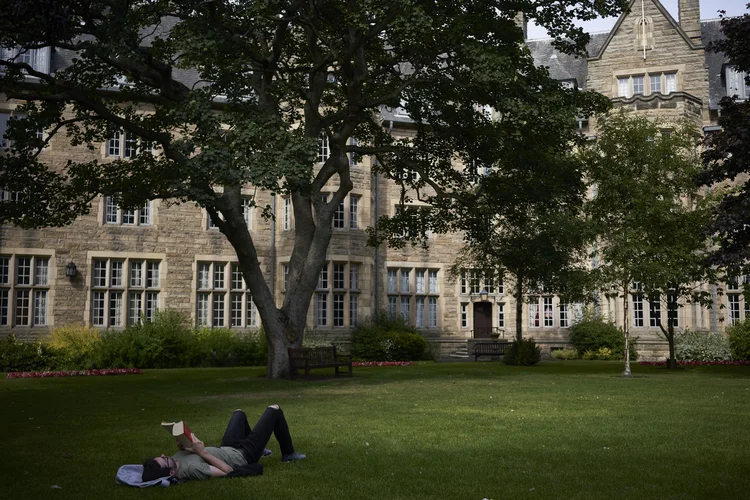 Um homem lê um livro fora do St. Salvator's Hall, uma residência estudantil da Universidade de St. Andrews, em St. Andrews, Escócia, em 14 de julho de 2018. A Universidade de St. Andrews, na Escócia, foi criticada por não renovar o contrato da diretora feminina de seu Instituto de Estudos de Gênero
 (David Azia/The New York Times)