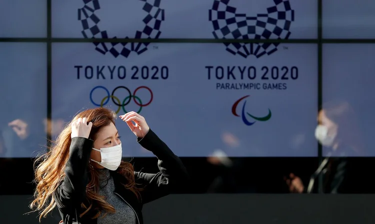 Moradora de Tóquio diante de cartaz dos Jogos Olímpicos (Issei Kato/Reuters)