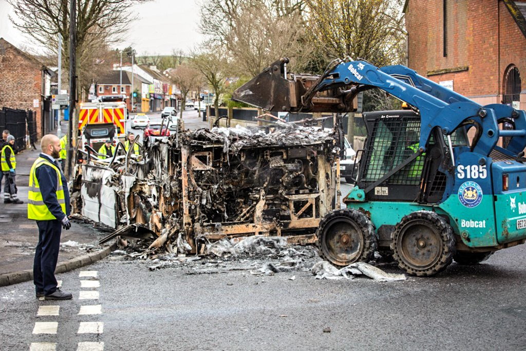 Funcionários retiram ônibus incendiado após noite de protestos e violência em Shankill Road, Belfast (PAUL FAIT/AFP)