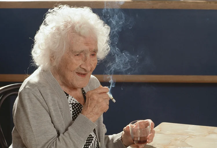 Jeanne Calment com seu cigarro diário e uma taça de vinho tinto por ocasião de seu 117º aniversário (Jean-Pierre Fizet/Getty Images)