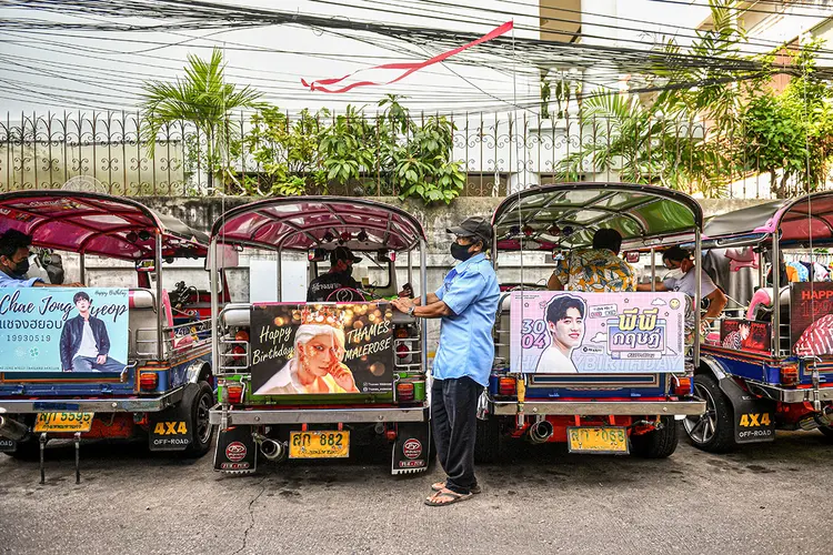 Motorista de tuk-tuk aguarda por clientes, em meio a veículos decorados com banners de astros tailandeses e sul-coranos. (Chalinee Thirasupa/Reuters)