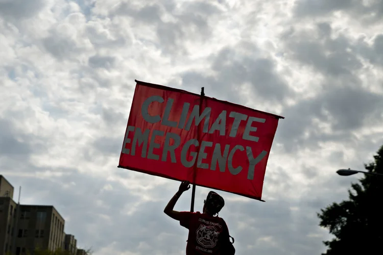 Um manifestante segura uma placa que diz "Emergência climática" enquanto bloqueia um cruzamento durante a manifestação climática "Shut Down DC" em Washington, D.C., EUA, na segunda-feira, 23 de setembro de 2019 (Andrew Harrer/Bloomberg)