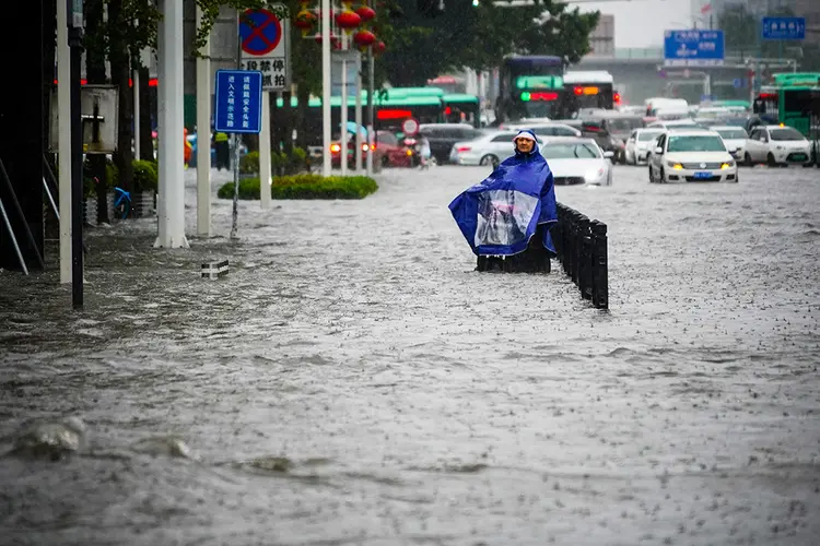 Morador com capa de chuva caminha por rua inundada em Zhengzhou, na província chinesa de Henan
20/07/2021 via REUTERS (Cnsphoto/Reuters)