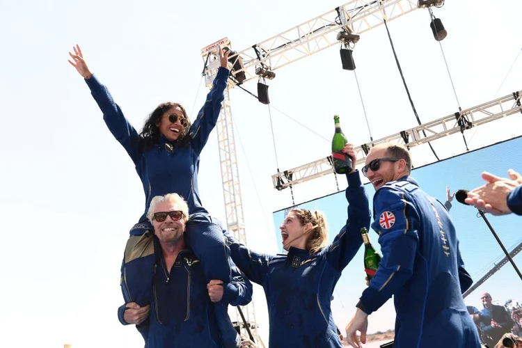 O fundador da Virgin Galactic, Richard Branson, com Sirisha Bandla nos ombros, aplaude os membros da tripulação após voar para o espaço a bordo de um Virgin Galactic, em 11 de julho de 2021 (Patrick T. FALLON / AFP/Getty Images)