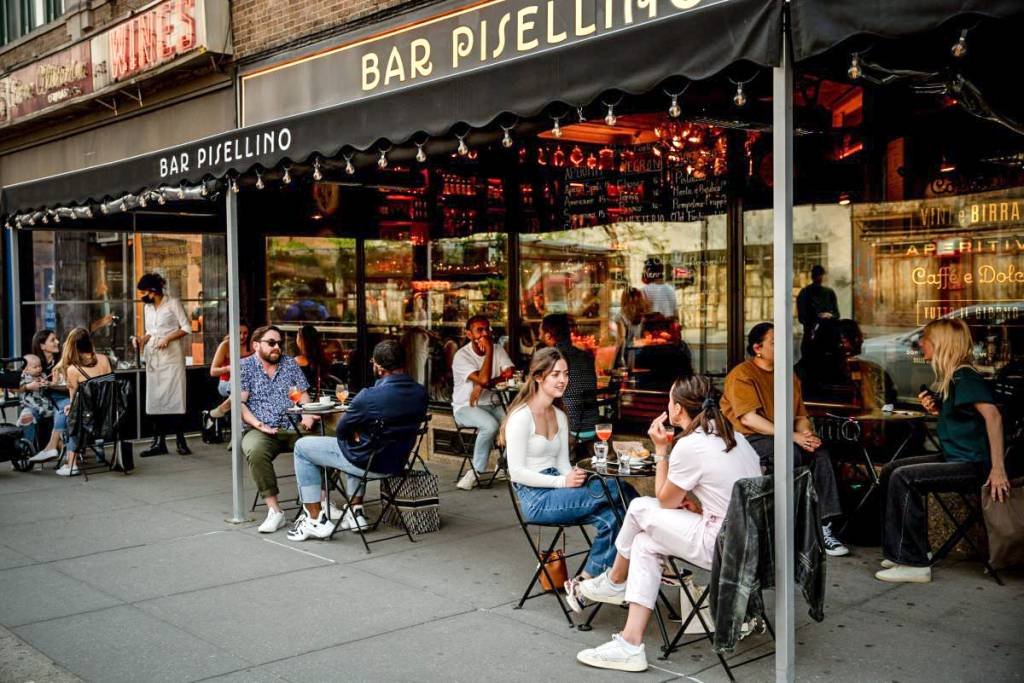Bar com clientes atendidos na calçada no bairro de West Village, em Nova York; tese de reabertura da economia ganha força novamente na bolsa | Foto: Amir Hamja/Bloomberg (Amir Hamja/Bloomberg)
