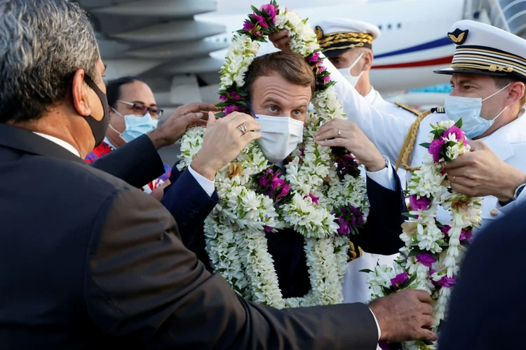 O presidente francês Emmanuel Macron (ao centro) é envolto em guirlandas ao ser saudado na pista ao chegar ao Aeroporto Internacional de Faa'a para uma visita ao Taiti, na Polinésia Francesa. (AFP/AFP)