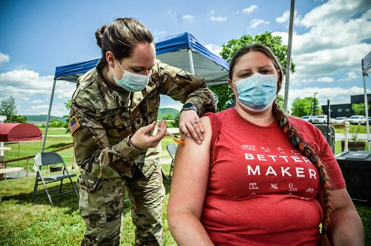 Um funcionário recebe uma vacina contra a Covid-19 de um soldado da Guarda Nacional em um posto de vacinação na Vermont Creamery em Websterville, Vermont, em 29 de junho de 2021. - Vermont - conhecido por Bernie Sanders, o primeiro Ben and Jerry's e folhagem dourada de outono - tem uma nova reivindicação à fama: o estado mais vacinado da América contra a Covid-19. Lar de casas de fazenda vermelhas e placas de advertência aos motoristas de alces, o segundo estado menos populoso dos Estados Unidos recentemente se tornou o primeiro a vacinar parcialmente 80% dos residentes qualificados. (Ed JONES/AFP)