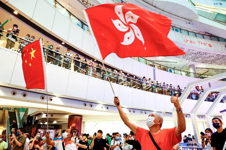 Homem comemora com bandeira de Hong Kong a medalha de prata da nadadora Siobhan Haughey ao lado de manifestantes pró-China em um shopping de Hong Kong nesta sexta (30). (Tyrone Siu/Reuters)
