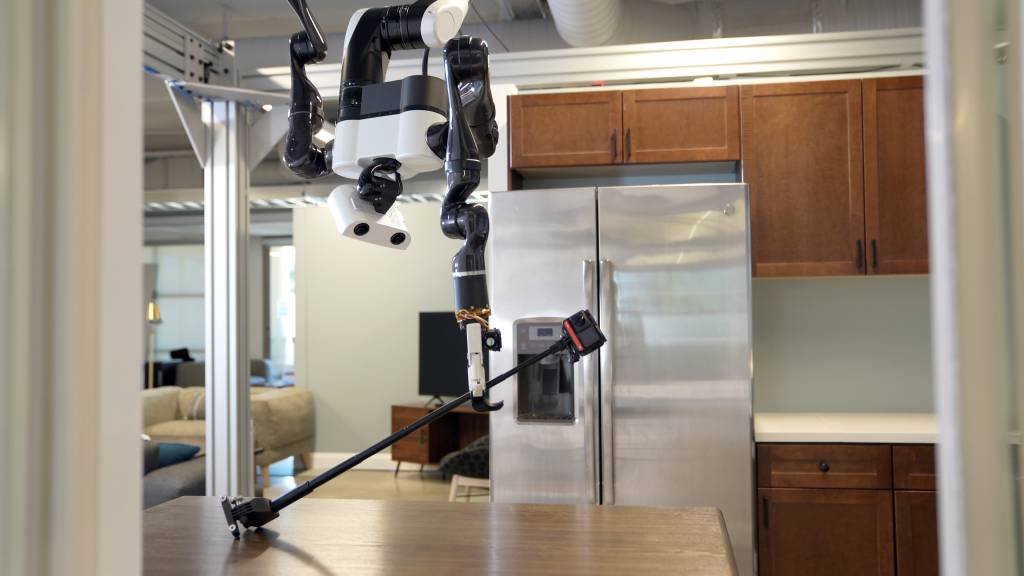 Robô doméstico desenvolvido pelo instituto de pesquisa da Toyota suspenso no teto e segurando câmera com braço (Toyota Research Institute/Reprodução)