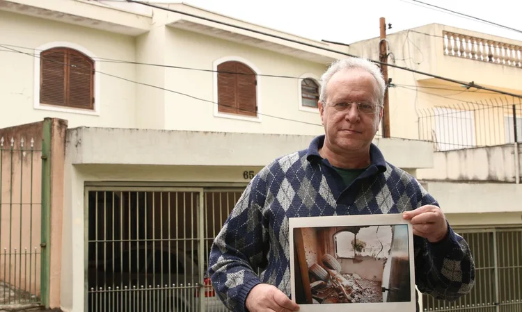 O jornalista Jorge Tadeu da Silva, um dos afetados pelo acidente com o avião modelo Fokker 100 da TAM que vitmou 99 pessoas em 1996, segura foto de como ficou a casa dele na rua Luís Orsini de Castro, no Jabaquara (Rovena Rosa/Agência Brasil)