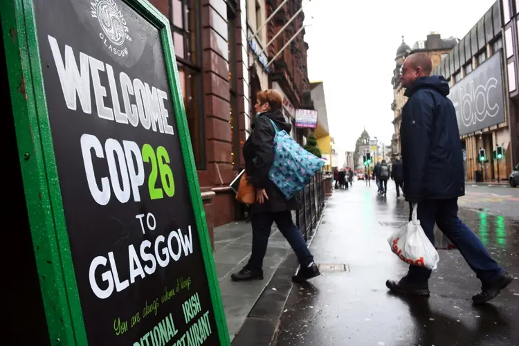 Pessoas entram em um bar passando por uma placa da COP26 no centro da cidade de Glasgow, Escócia, em 29 de outubro de 2021 (Agence France-Presse/AFP)