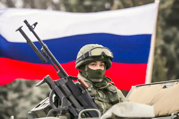 Um ativista pró-Rússia segura uma bandeira russa atrás de um militar armado no topo de um veículo do exército russo, próximo a um posto de controle de fronteira na cidade de Balaclava, na Crimeia (Baz Ratner/Reuters)