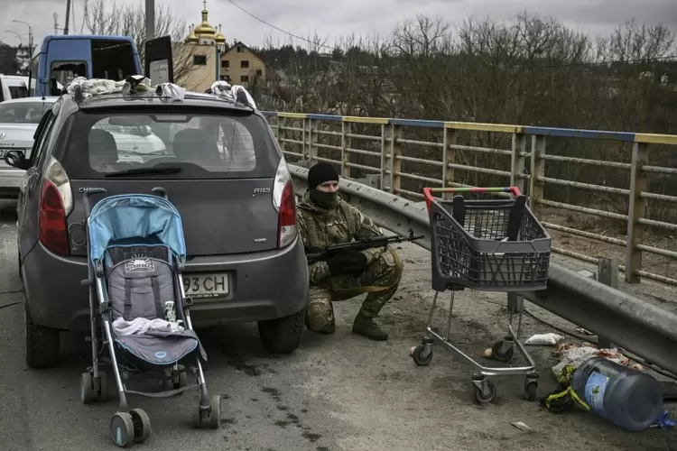 Soldado ucraniano se protege atrás de automóvel em Irpin, onde jornalista dos EUA foi morto a tiros (Dmitry ZAKS/AFP)