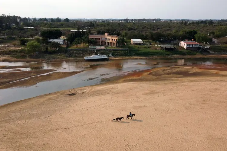 In this aerial view a man rides a horse along the river bed backgrounded by a stranded vessel on a dry arm of the Parana River, which water level reached a historic low, in Goya, Corrientes, Argentina, on August 21, 2021. - The Parana River, which runs through Brazil, Paraguay and Argentina, the tenth largest river basin in the world, has reached its lowest water level in over half a century and it is an enigma whether it is a natural cycle or a result of climate change, with uncertain long-term effects. (Photo by JUAN MABROMATA / AFP) (Photo by JUAN MABROMATA/AFP via Getty Images) (JUAN MABROMATA/Getty Images)