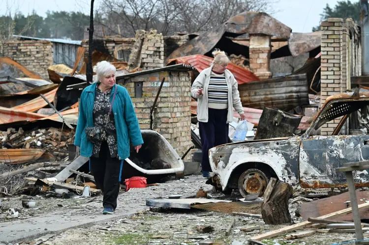 Duas mulheres passam por escombros em Mochchun, Ucrânia, em 20 de abril de 2022. (AFP/AFP)