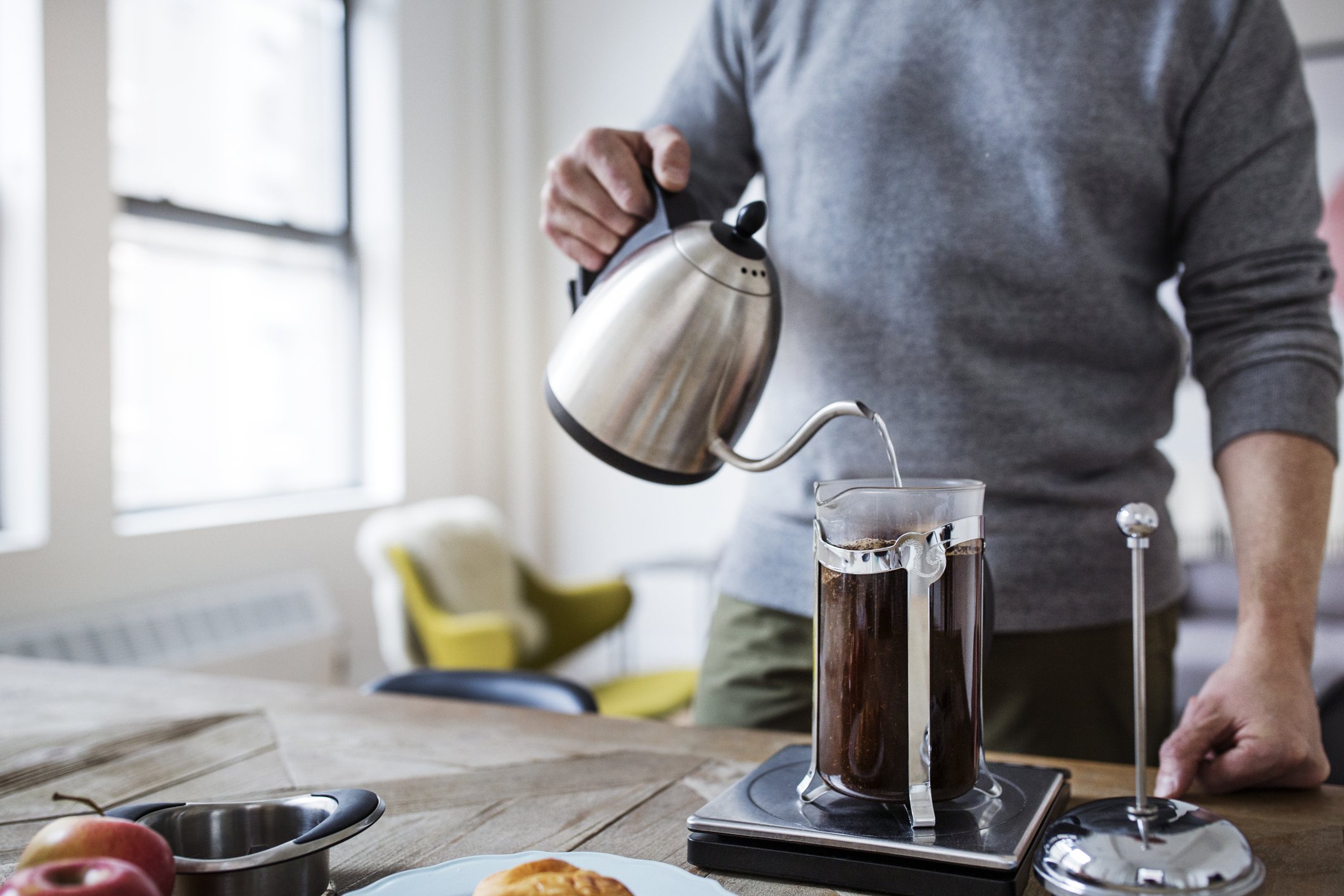 Midsection of man pouring water in French press while preparing coffee at home