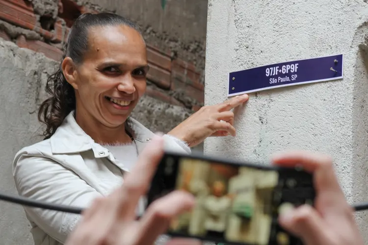 Alexandra Pereira Silva, de 46 anos, ao lado de placa com o seu primeiro endereço que aparece no Google Maps (André Silva/ Cria Brasil/Reprodução)