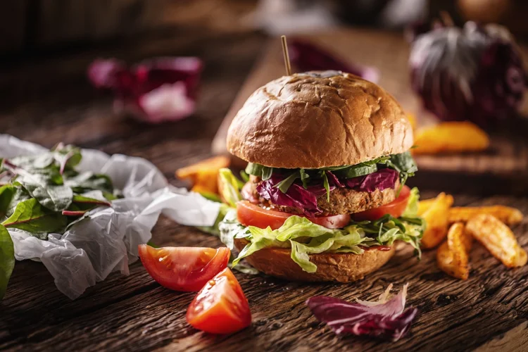 Healthy veggie burger with vegan patty, fresh tomatoes, lettuce and potatofries served on wooden desk. (SimpleImages/Getty Images)