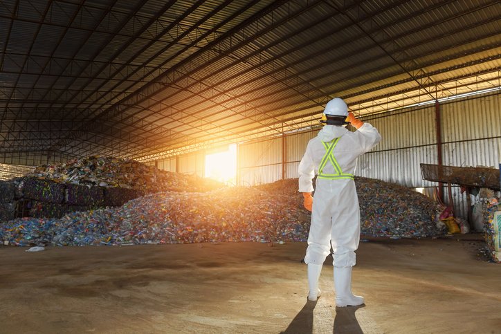 Rear view of a manual worker at a recycling plant wearing biohazard suit, Thailand