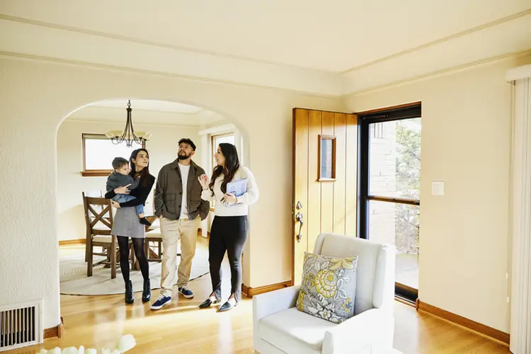 Wide shot for family with toddler in discussion with real estate agent while looking home for sale during open house (Getty/Getty Images)