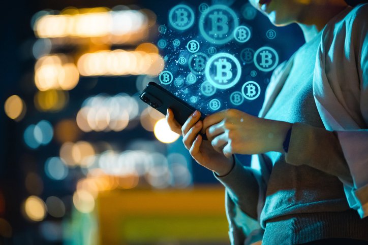 Mid-section of young Asian woman using smartphone in city at night, against illuminated street lights bokeh, working with Bitcoin technologies, investing or trading Bitcoin on cryptocurrency. Business on the go (Getty/Getty Images)