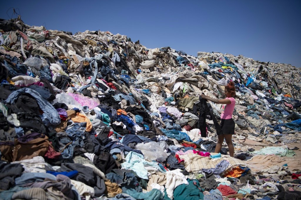 Mulher procura roupas usadas em montanha de resíduos têxteis despejados no deserto do Atacama (AFP/AFP)