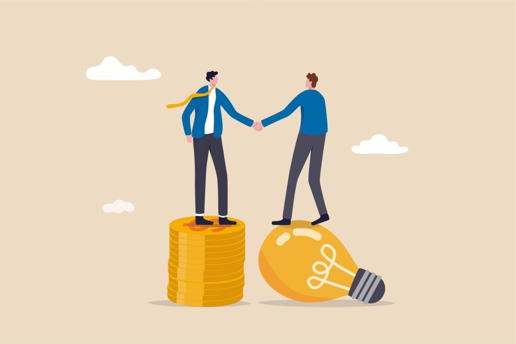 Idea pitching, fund raising and venture capital, selling business or merger agreement concept, entrepreneur businessman standing on lightbulb idea lamp shaking hands with VC on money coins stack. (Nuthawut Somsuk/Getty Images)