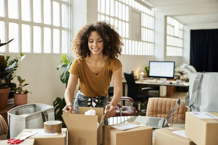 Confident businesswoman packing boxes at table. Young female entrepreneur is working at home office. She is in casuals. (Morsa Images/Getty Images)