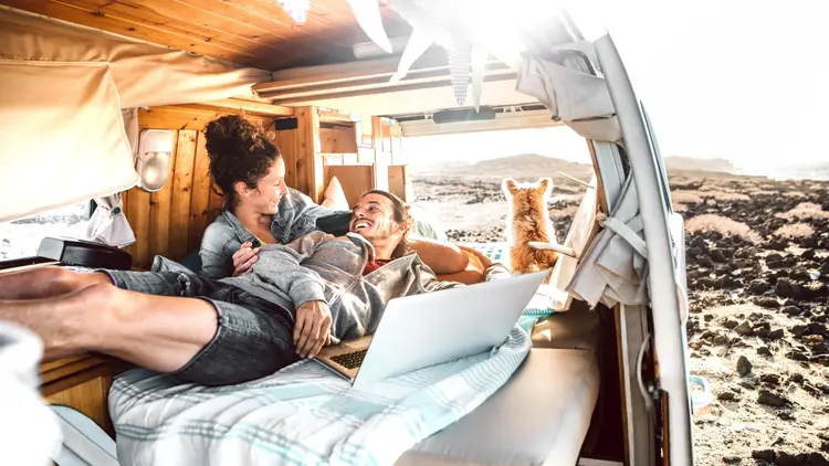 Hipster couple with dog traveling together on retro mini van transport - Digital nomad concept with indie people on minivan romantic trip working at laptop pc in relax moment - Warm contrast filter (ViewApart/Getty Images)