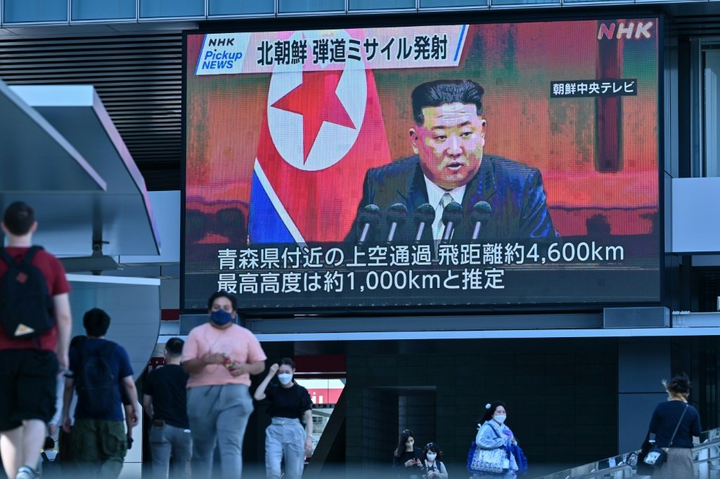 Transeuntes caminham sob uma tela grande com uma imagem do líder norte-coreano Kim Jong Un em Tóquio em 4 de outubro de 2022. (AFP/AFP Photo)