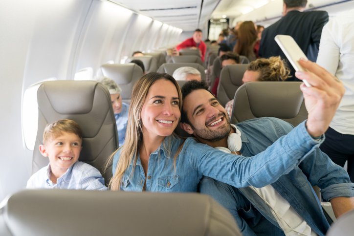 Happy family traveling by plane and taking a selfie with a cell phone while smiling - travel concepts (Hispanolistic/Getty Images)