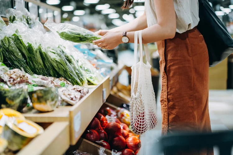 Cropped shot of young Asian woman shopping for fresh organic groceries in supermarket. She is shopping with a cotton mesh eco bag and carries a variety of fruits and vegetables. Zero waste concept (d3sign/Getty Images)