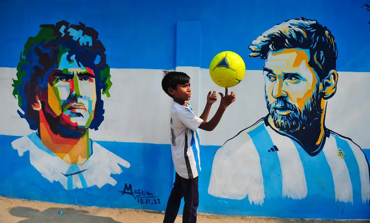 SYLHET, BANGLADESH - DECEMBER 14: A young Argentina fan poses in front of a mural of Lionel Messi, after Argentinas win over Croatia in the semi-final to qualify for the World Cup Final. Bangladesh has never qualified for any football world cup, but has great love for football and has huge fan followings for both Argentina and Brazil. On December 14, 2022 in Sylhet, Bangladesh. (Photo credit should read Md Rafayat Haque Khan/ Eyepix Group/Future Publishing via Getty Images) (Future Publishing/Getty Images)
