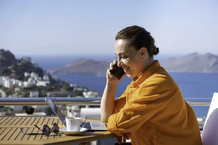 Woman working from beautiful terrace above the sea. Working from home. Working from vacation. (RainStar/Getty Images)