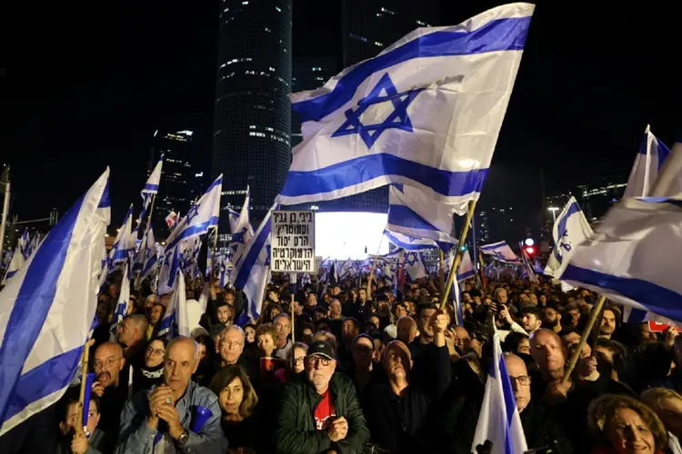 Ativistas erguem cartazes e faixas enquanto se manifestam a favor da decisão do Parlamento, em Tel Aviv (AFP/AFP)