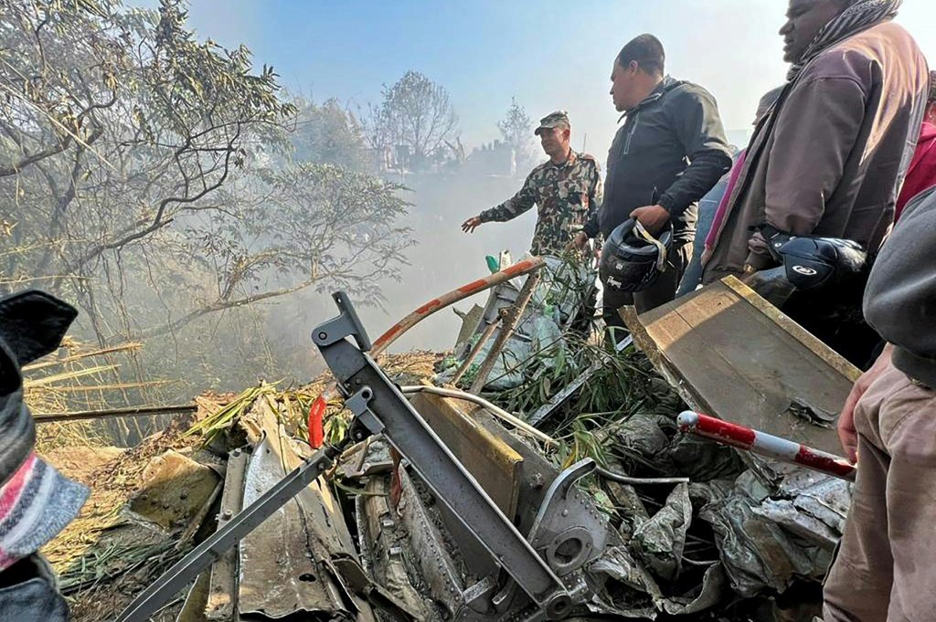 Equipes de resgate ficam ao lado dos destroços do avião, com 72 pessoas a bordo, que caiu em Pokhara, no Nepal. (AFP/AFP)